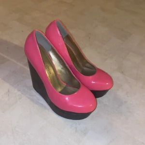 Rosa kilklackar - Snygga rosa kilklackar med hög platå och rundad tå. Perfekta för att ge lite extra höjd och stil till din outfit. Den rosa färgen ger en pop av färg och gör dem till ett statement-piece.