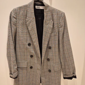 Rutig kavaj från Zara - Snygg rutig kavaj från Zara i grå och bruna toner. Kavajen har en klassisk design med knappar framtill och långa ärmar. Perfekt för en stilren look.
