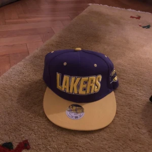 Lila och gul Lakers keps - Snygg Lakers keps i lila och gult med broderad logga framtill. Perfekt för basketfans som vill visa sitt stöd. Kepsen har en platt skärm och justerbar passform.