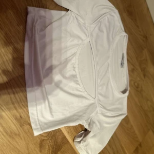 Vit kortärmad topp med cut-out detalj - Säljer en stilren vit topp med korta ärmar och en trendig cut-out detalj framtill. Perfekt för en modern och avslappnad look. Toppen är gjord i ett mjukt och bekvämt material.