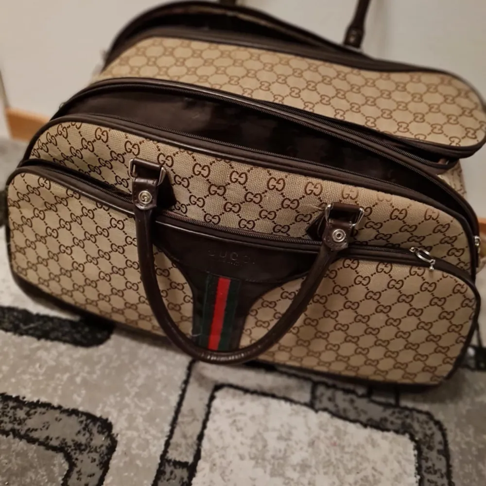Säljer en snygg beige och brun resväska från Gucci med det klassiska GG-mönstret. Väskan har två handtag och en dragkedja för säker förvaring. Den har också de ikoniska gröna och röda ränderna framtill. Perfekt för resan! Nypris runt 16500kr.. Laukut & Käsilaukut.