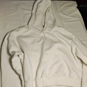 Vit hoodie från Puma - Säljer en stilren vit hoodie från Puma. Den har en klassisk design med en justerbar huva och ribbade muddar vid ärmslut och nederkant. Perfekt för en avslappnad look. 🐾