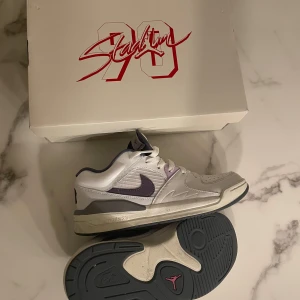 Nike Air sneakers  - Snygga Nike Air sneakers i vitt med lila detaljer och snörning. Skorna har en klassisk design med 'AIR' tryckt på hälen och en robust sula för extra komfort. Perfekta för en stilren look.