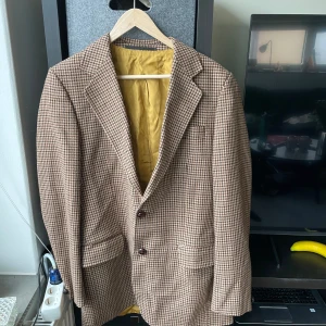 Kunglig svensk tillverkad kavaj med guldfoder retro - Retro rutig kavaj med klassiskt mönster i brunt och beige. Kavajen har två knappar framtill och ett elegant guldfärgat foder. Gjord i Sverige och ger retro vibbar. Köpt i Göteborg!!          Ärmlängd från axel: 64 cm Från till axel: 44 cm Kavajens längd: 81 cm