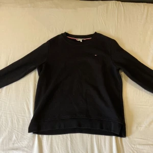 Svart tröja från Tommy Hilfiger - Säljer en stilren svart tröja från Tommy Hilfiger med deras ikoniska logga broderad på bröstet. Tröjan har långa ärmar och en klassisk rund halsringning. Perfekt för en avslappnad och snygg look.