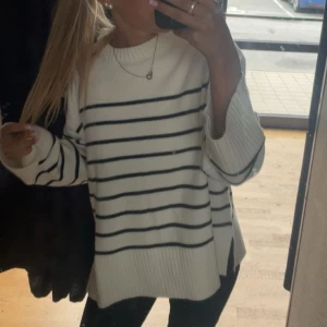 Vit och svart randig tröja - Säljer en stilren vit tröja med svarta ränder. Tröjan har långa ärmar och en avslappnad passform med ribbade muddar vid ärmslut och nederkant. 