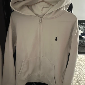 Vit zip hoodie från Ralph Lauren - Tjena säljer min vita zip hoodie från polo Ralph lauren, skick 9-10 ända är att jag tog av snörena annars är den perfekt, ny pris ca 2100 kr mitt pris 950 kr vill du ha byxorna till hela tracksuiten gå in på mitt konto, använd ca 2 gånger kommer inte till användning därför säljer jag den, är du intresserad så är de bara höra av sig🙌🏼
