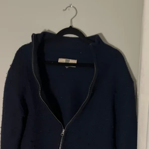 Mörkblå stickad zip tröja från Bertoni - Säljer en mörkblå stickad jacka från Bertoni med dragkedja framtill. Jackan har en enkel och stilren design, perfekt för kyligare dagar. Den är långärmad och har en mjuk och bekväm känsla.