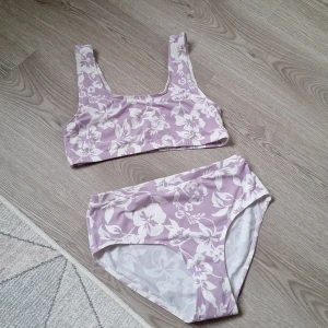 Bikini - En lila bikini med vita blommor. Den är aldrig använd, köpt rabatterad, den har små fläckar som man kan se på bild 4 men det är inget som syns från avstånd.  Den är I storlek 158-164/ 12-14y. 