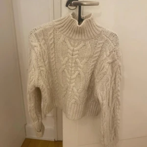 Vit stickad tröja från MNG - Säljer en mysig vit stickad tröja från Mango. Tröjan har en hög krage och långa ärmar, perfekt för kyliga dagar. Den är croppad och ger en trendig look. Har bara använt en gång.