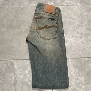  Nudie Jeans Tube Kelly  - Snygga blå jeans från Nudie Jeans med klassisk femficksdesign och subtila slitningar. De har en knappgylf och är tillverkade i ett slitstarkt denimtyg. Perfekta för en avslappnad stil. Modellen är Tube Kelly