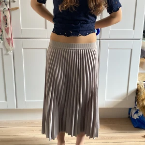 Grå plisserad kjol från H&M - Snygg grå plisserad kjol från H&M i en elegant och flytande design. Kjolen har en elastisk midja för extra komfort och en stilren look som passar perfekt till olika tillfällen. Perfekt för dig som vill ha en chic och bekväm stil. Storlek s/m