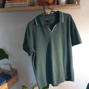 Grön pikétröja från George - Säljer en stilren grön pikétröja från George. Tröjan har korta ärmar och en klassisk krage med vita detaljer. Perfekt för en avslappnad och snygg look. Storlek M.