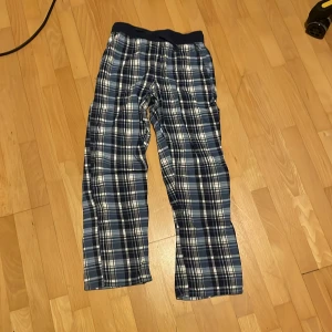 Rutig byxa från Kappahl - Säljer ett par bekväma och stiliga rutiga byxor från Kappahl. Byxorna har en elastisk midja och är i en snygg kombination av blått, vitt och svart. Perfekta för en avslappnad dag hemma eller som mysbyxor.