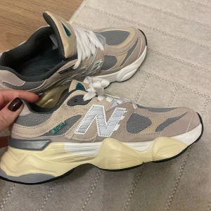 Beige och grå sneakers.  - Säljer ett par snygga lik  New Balance sneakers i beige och grått med vita detaljer. Skorna har en chunky sula och klassisk snörning. Perfekta för en stilren och bekväm look. Dock små i storlek skulle säga 38