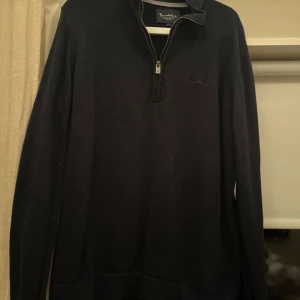 Svart tröja med dragkedja från Bondenid - Säljer en stilren svart tröja från Bondenid med dragkedja och broderad logga på bröstet. Perfekt för en klassisk look. Tröjan har långa ärmar och en bekväm passform.