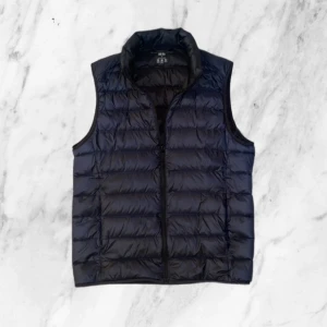 Marinblå dunväst från Uniqlo - Säljer en stilren mörkblå dunväst från Uniqlo. Västen är ultralätt och har en funktion där man kan packa ned den i en liten påse (som följer med på köpet) Perfekt för lager-på-lager under kyliga dagar. Passar bra för både höst och vår . Skick: 9/10✅ Hör av er vid funderingar!