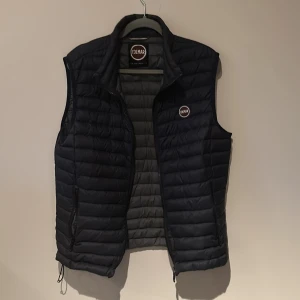  Colmar Väst - Säljer en svart dunväst från Colmar med dragkedja och quiltad design. Perfekt för kyliga dagar och enkel att matcha med andra plagg. Liten defekt på ryggen men inget som märks