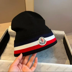 Moncler Tricolour Beanie Mössa - Säljer en Moncler Tricolour beanie, en stilren och exklusiv mössa i fin ullkvalitet. Mössan har Monclers klassiska design med trikolorfärger och det ikoniska logotypmärket framtill. Perfekt för dig som vill kombinera värme och lyxig stil under vintersäsongen.  Vid intresse eller frågor, skicka ett meddelande!
