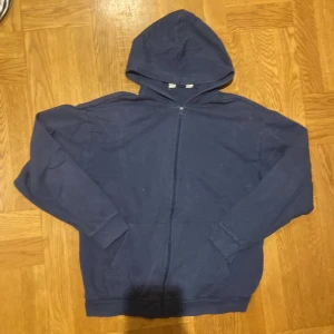 Mörkblå full-zip hoodie från H&M - Säljer en mörkblå hoodie från H&M med dragkedja framtill. Tröjan har en klassisk design med huva och långa ärmar. Perfekt för en avslappnad stil. Grisch full zip