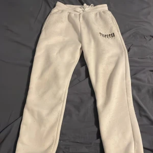Vita mjukisbyxor från Trapstar - Säljer ett par bekväma vita mjukisbyxor från Trapstar. Byxorna har en elastisk midja med snörning och en tryckt logga på ena benet. Perfekta för en avslappnad stil.