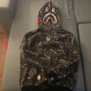 Bape Hoodie - Svart/Grå Bape Hoodie som jag säljer pga att jag ändrat stil på garderob. Den är i fantastiskt skick och har inte något slitage. Storleken är L på tröjan men den passar mer för folk med S. Vid fler frågor kontakta mig via Plick!
