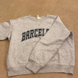 Grå sweatshirt med Barcelona-tryck - Säljer en grå sweatshirt med texten 'Barcelona' i mörkblått på bröstet. I storlek S🫶🏼
