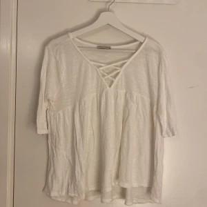 Vit topp från Angelology - Säljer en vit topp från Angelology med trekvartsärm och en snygg snörning vid halsen. Perfekt för en avslappnad stil. Toppen har en lös passform och är tillverkad i ett mjukt material.