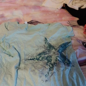 Ljusblå t-shirt med stjärnmönster - Säljer en ljusblå t-shirt från bpc med ett stort stjärnmönster i mörkare blå nyanser. T-shirten har korta ärmar och en rund halsringning. Perfekt för en avslappnad stil.