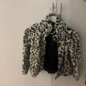 Svartvit pälsjacka - Snygg svartvit pälsjacka med djärvt mönster. Jackan har långa ärmar och stängs med knappar framtill. Strl. 128