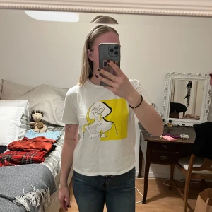 Vit t-shirt med konstnärligt tryck - Snygg vit t-shirt med ett unikt konstnärligt tryck i svart och gult på framsidan. Perfekt för en avslappnad stil med en kreativ touch.