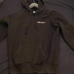 Svart hoodie från Champion - Säljer en klassisk svart hoodie från Champion i storlek medium. Den har en känguruficka framtill och justerbar huva med dragsko. Perfekt för en avslappnad stil.