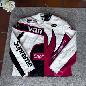 Flerfärgad skinnjacka från Supreme x Yohji Yamamoto - Unik skinnjacka i rött, svart och vitt från Supreme x Yohji Yamamoto. Jackan har en cool design med tryck och logotyper, samt en hög krage och dragkedja framtill. Perfekt för dig som vill sticka ut!