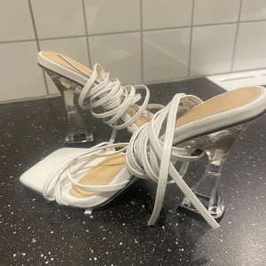 Vita klackskor med transparent klack - Oanvända vita klackskor med transparent klack och knytband upp mot vaden (går att knyta på flera olika sätt) storlek 38