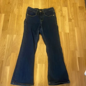 Mörkblå bootcut jeans från 77th Flea - Säljer ett par snygga mörkblå bootcut jeans från 77th Flea. De har en klassisk femficksdesign och är perfekta för en avslappnad stil. Jeansen har en bekväm passform och är tillverkade i ett slitstarkt material.