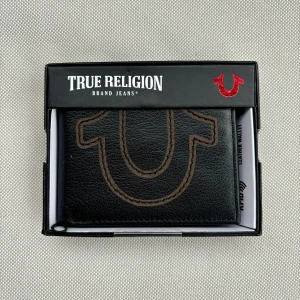 Svart plånbok från True Religion - Snygg svart plånbok i skinn från True Religion med ikoniska logotypen på framsidan. Kartongen ingår. 