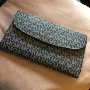 Mörkblå plånbok - Snygg grå plånbok från Michael Kors med monogrammönster. Plånboken har flera fack för kort och en dragkedja för mynt. Plånboken är i bra använt skick. Säljer på grund av att jag inte använder plånbok.