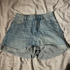 Blå jeansshorts från H&M - Snygga blå jeansshorts från H&M med hög midja och klassisk femficksdesign. Perfekta för sommardagar med en avslappnad stil. De har en knapp och dragkedja framtill samt uppvikta benslut.