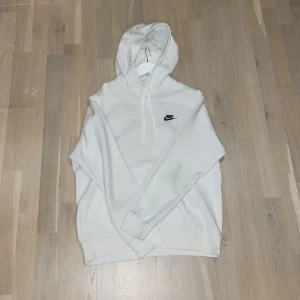 Vit hoodie från Nike - Säljer en stilren vit hoodie från Nike med klassisk logga på bröstet. Tröjan har en bekväm passform och är perfekt för vardagsbruk. Den har en justerbar huva och ribbade muddar vid ärmslut och nederkant. Väldigt fin tröja utan fläckar eller skador 