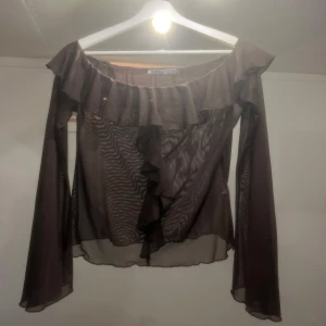 Brun blus med volangdetaljer - Säljer en elegant brun blus med volangdetaljer och långa ärmar från NAKD i stl S. Blusen har en offshoulder-design och är tillverkad i ett lätt och luftigt material. Perfekt för en stilfull look. Använd ca 2 gånger