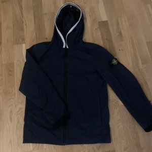   Stone island windbreaker - Snygg mörkblå jacka från Stone Island Junior med huva och dragkedja. Jackan har en ikonisk stone island  logga på ärmen och är perfekt för en stilren look. Den är designad för att ge en bekväm passform och skydda mot väder och vind. Den är i storlek 152-164cm. Nypris 2499. PRIS KAN DISKUTERAS I DM! 