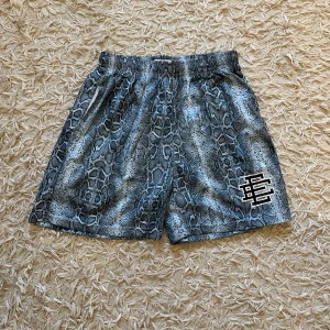 Eric Emmanuel ”snake skin” shorts - Hej! Säljer dessa helt nya Eric Emmanuel ”snake skin” shorts-  pga för stor storlek. Dessa är ej äkta, de är väldigt snygga med inte autentiska och därför säljer jag billigt. Notera att de är väldigt fina och perfekta för sommaren. De är inte ”genomskinliga” och relativt bra kvalitet. De är storlek L men passar mer som M. Köpta i Turkiet för 35 euro. Hör av er vid minsta intresse! 