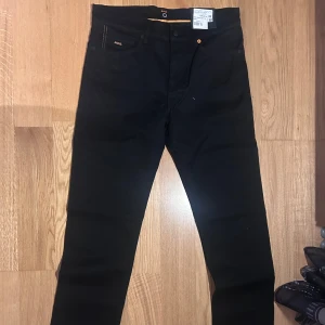 Svarta slim fit jeans från Boss - HELT NYA snygga svarta slim fit jeans från Boss. De har en klassisk design med fem fickor och orangea sömmar som ger en cool kontrast. Perfekta för en stilren look. NYPRIS är 1299. W31 L34. Modellen är 'MAINE.'