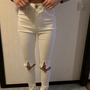 Vita skinny jeans med slitningar - Snygga vita skinny jeans med hög midja och slitningar på knäna. Perfekta för en trendig look. De har en klassisk femficksdesign och stängs med knapp och dragkedja.