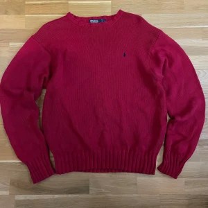 Röd stickad tröja från Polo Ralph Lauren - Säljer en snygg röd stickad tröja från Polo Ralph Lauren i 100% bomull. Tröjan har en broderad logga på bröstet och ribbade muddar vid ärmslut och nederkant. Perfekt för kyligare dagar! Större i storleken.