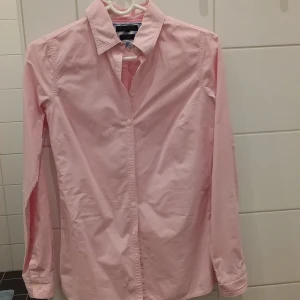 Rosa randig skjorta från Gant - Snygg rosa skjorta från Gant med diskreta ränder och klassisk krage. Skjortan har långa ärmar och knappar framtill. Perfekt för en stilren look.