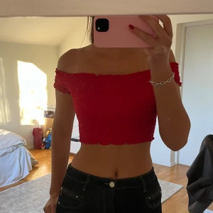 Röd offshoulder topp - Trendig röd offshoulder topp med smockdetaljer. Den är croppad och perfekt för sommarens varma dagar. Passar utmärkt till både jeans och kjol.