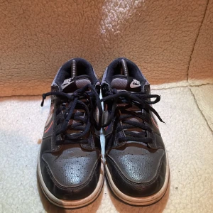 Nike sneakers i svart och grått - Snygga Nike sneakers i svart och grått med vita detaljer och snörning. Perfekta för en casual look. De har en klassisk design med Nike-loggan på sidan och baksidan, med en cool färgdesign. Skorna har små slitningar på snöringen. Pris kan diskuteras.