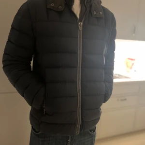 Colmar jacka - Snygg svart dunjacka från Colmar med dragkedja och huva. Jackan har en quiltad design och långa ärmar. Perfekt för kyliga dagar. 