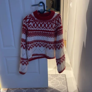 Röd och vit stickad tröja från H&M - Säljer en mysig röd och vit stickad tröja från H&M med ett traditionellt mönster. Tröjan har långa ärmar och en rund halsringning, perfekt för kyliga dagar. Använd 1 gång, köpt för 500.
